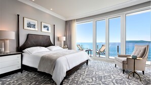 A hotel room with a large bed, a chair, a small table, and a view of the sea. - Royal Blue Hotel (Dubrovnik)