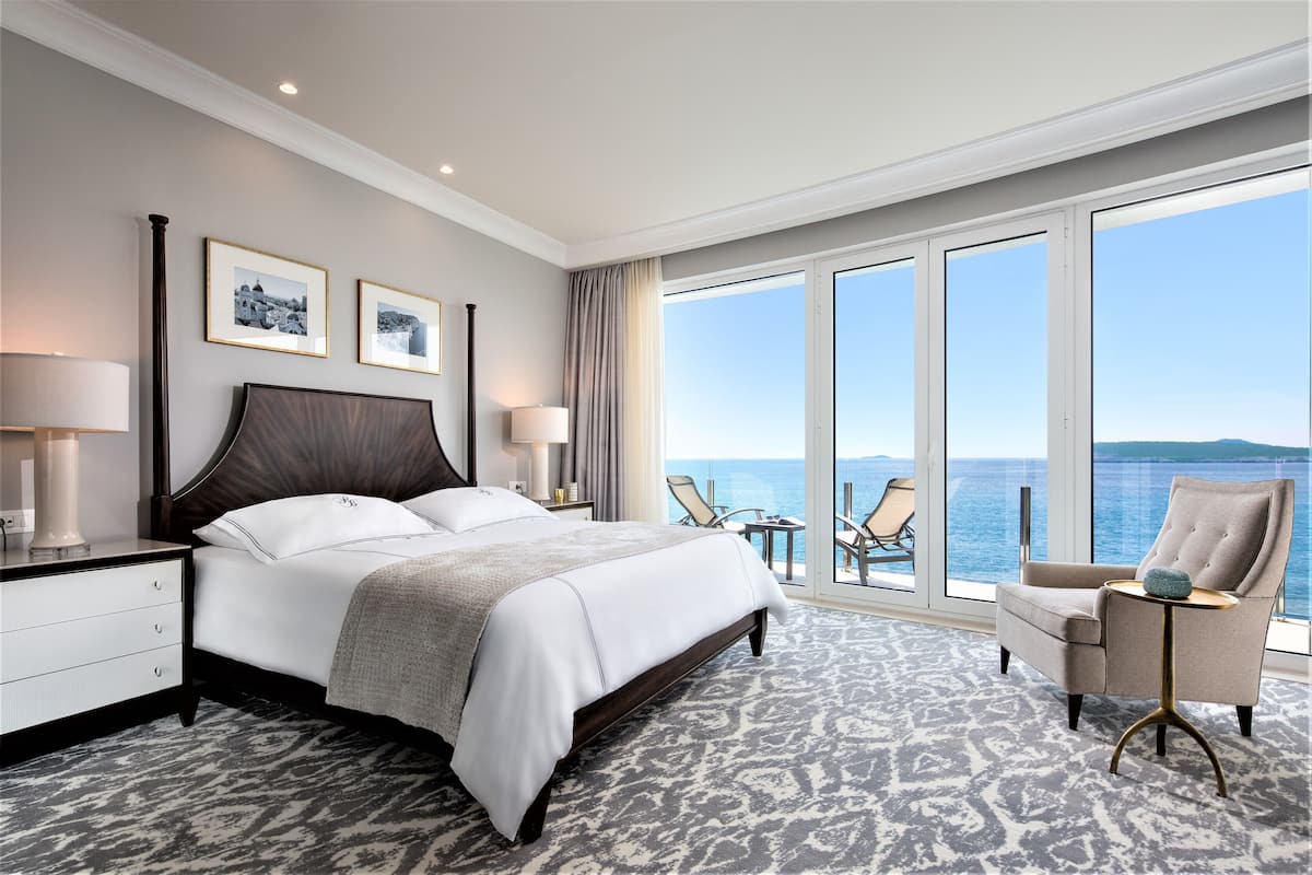 Habitación de hotel con una cama grande, una silla, una mesita y vistas al mar.