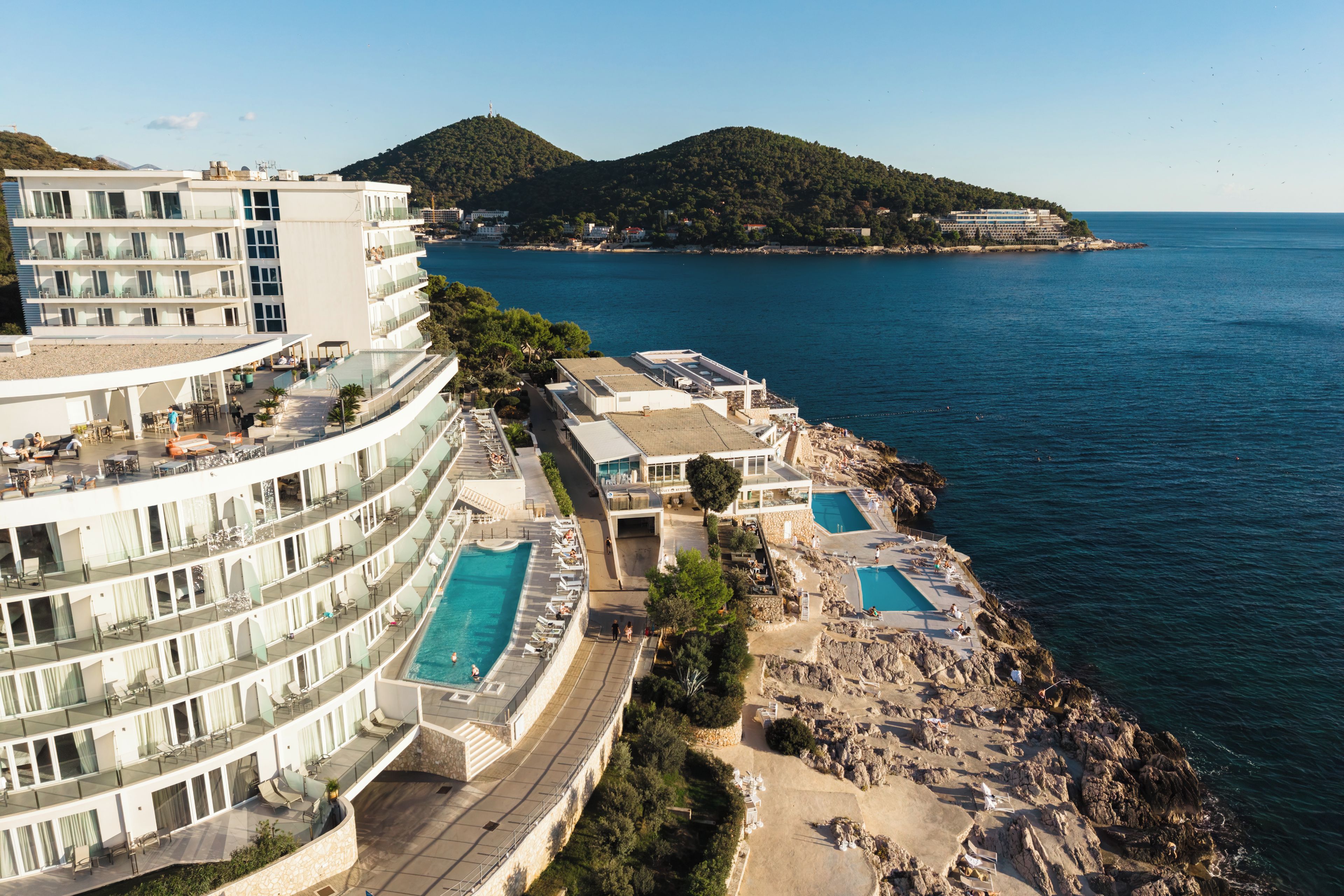 A resort with multiple swimming pools, a beach area, and a view of the sea and hills.