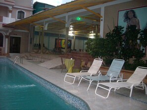 Un espace aménagé au bord de la piscine, avec des chaises longues, un coin salon abrité et une fresque murale.