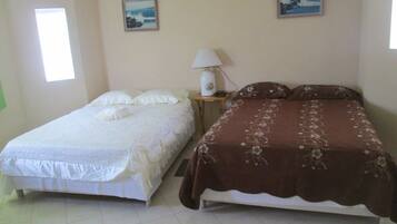 Two single beds with white and brown bedding, a small bedside table with a lamp, and two framed pictures on the wall.