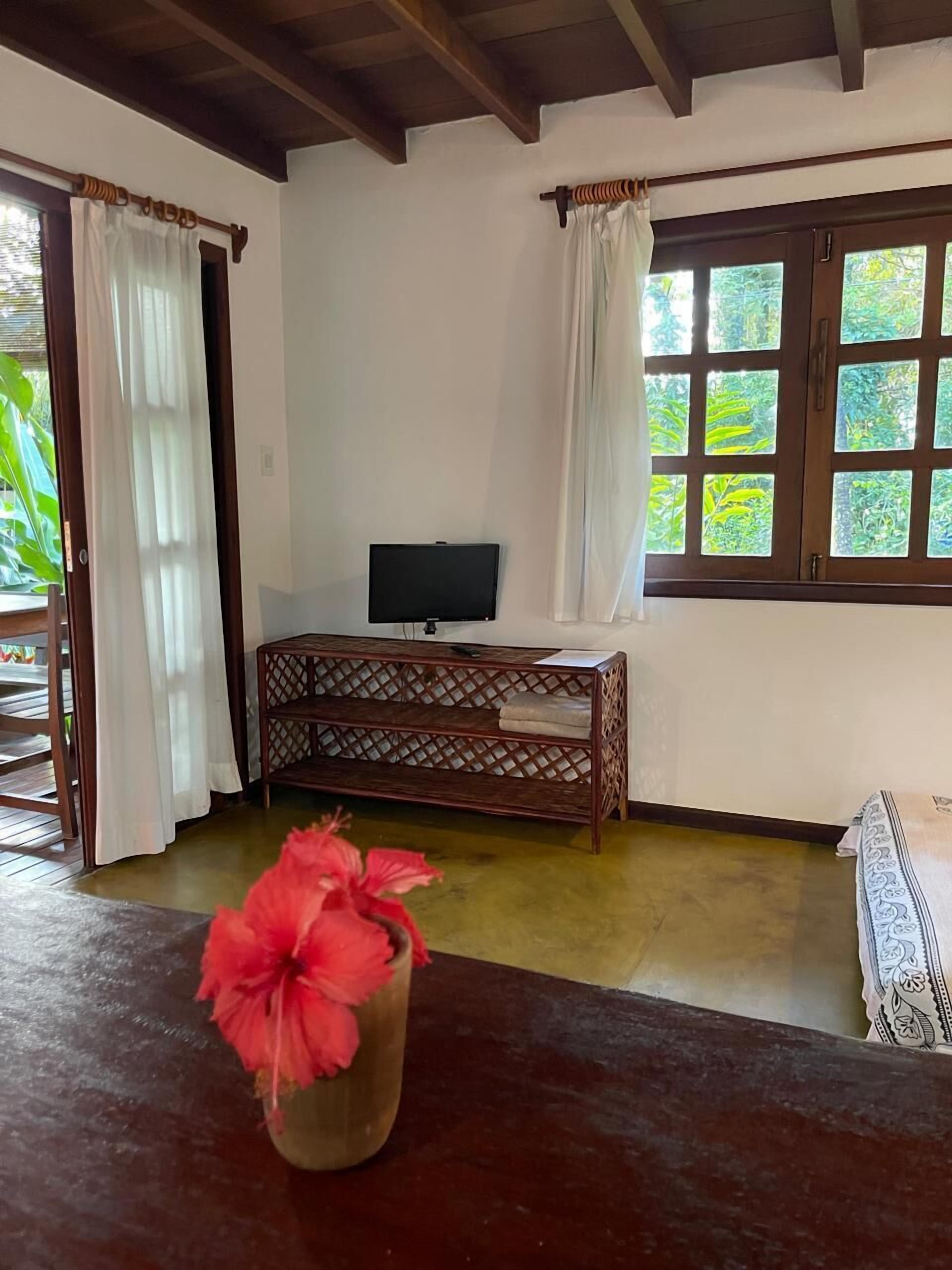 A room with a wooden bench, a TV on a stand, and a window with curtains.