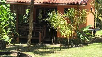 Uma casa de dois andares com telhado de telhas vermelhas, cercada por vegetação exuberante e palmeiras.
