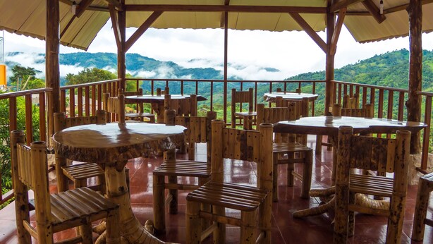 Una terraza de madera con mesas y sillas que da a un paisaje montañoso.