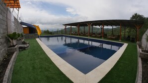Una piscina con tobogán, rodeada de césped artificial y una zona de estar cubierta.