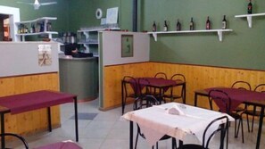 Interior de restaurante con paneles de madera, mesas blancas y rojas, y estanterías con botellas en la pared.