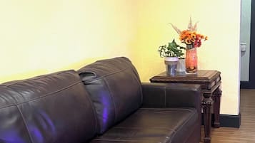 A black leather sofa in a hallway with wooden flooring, a small table with a vase of flowers, and a television mounted on the wall.