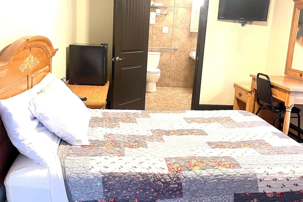 Ein Hotelzimmer mit einem Bett, einem Fernseher, einem Spiegel und einem durch eine geöffnete Tür einsehbarer Badezimmer.