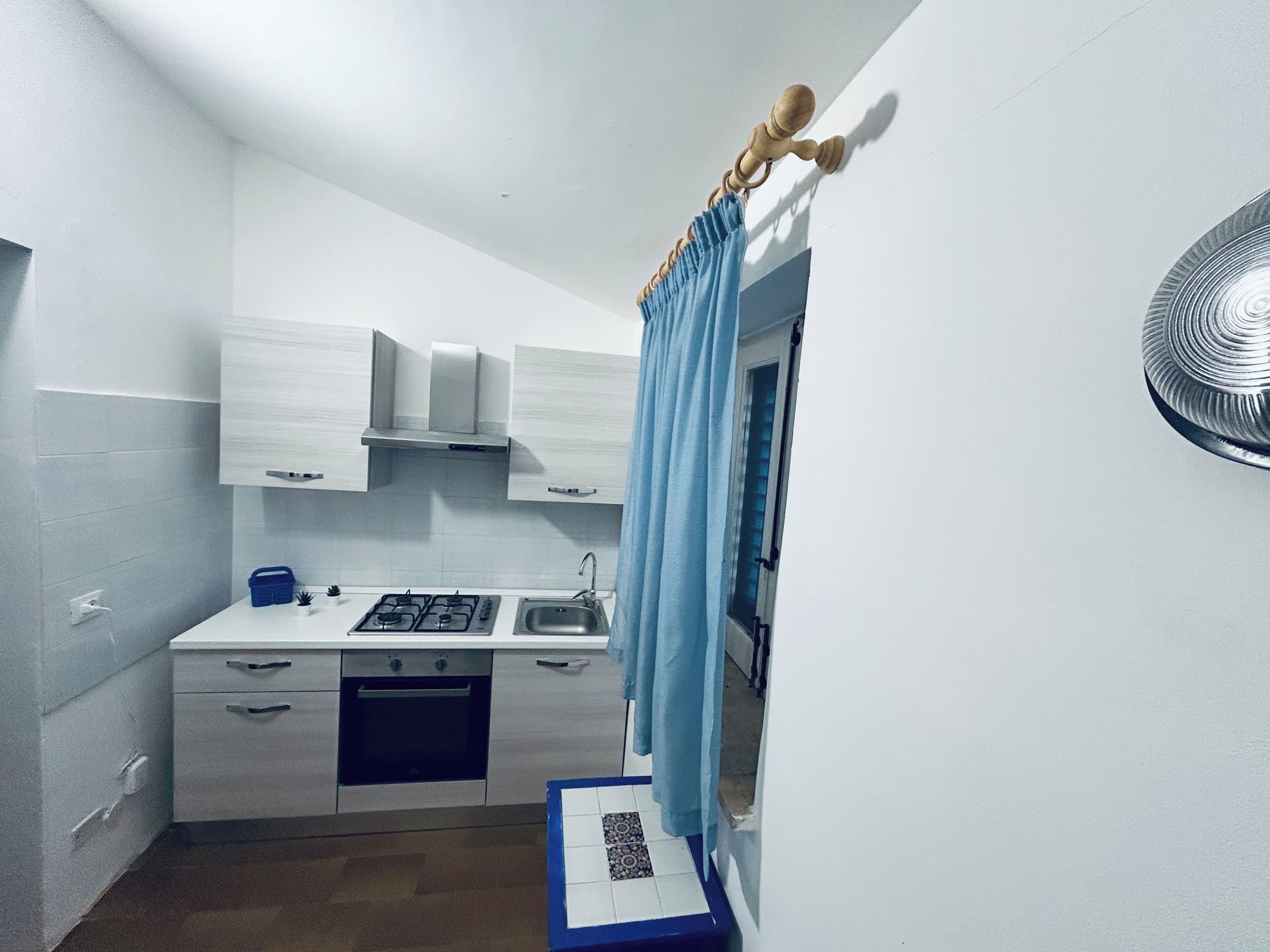 A compact kitchen with white cabinets, a gas stove, a sink, and a blue curtain.