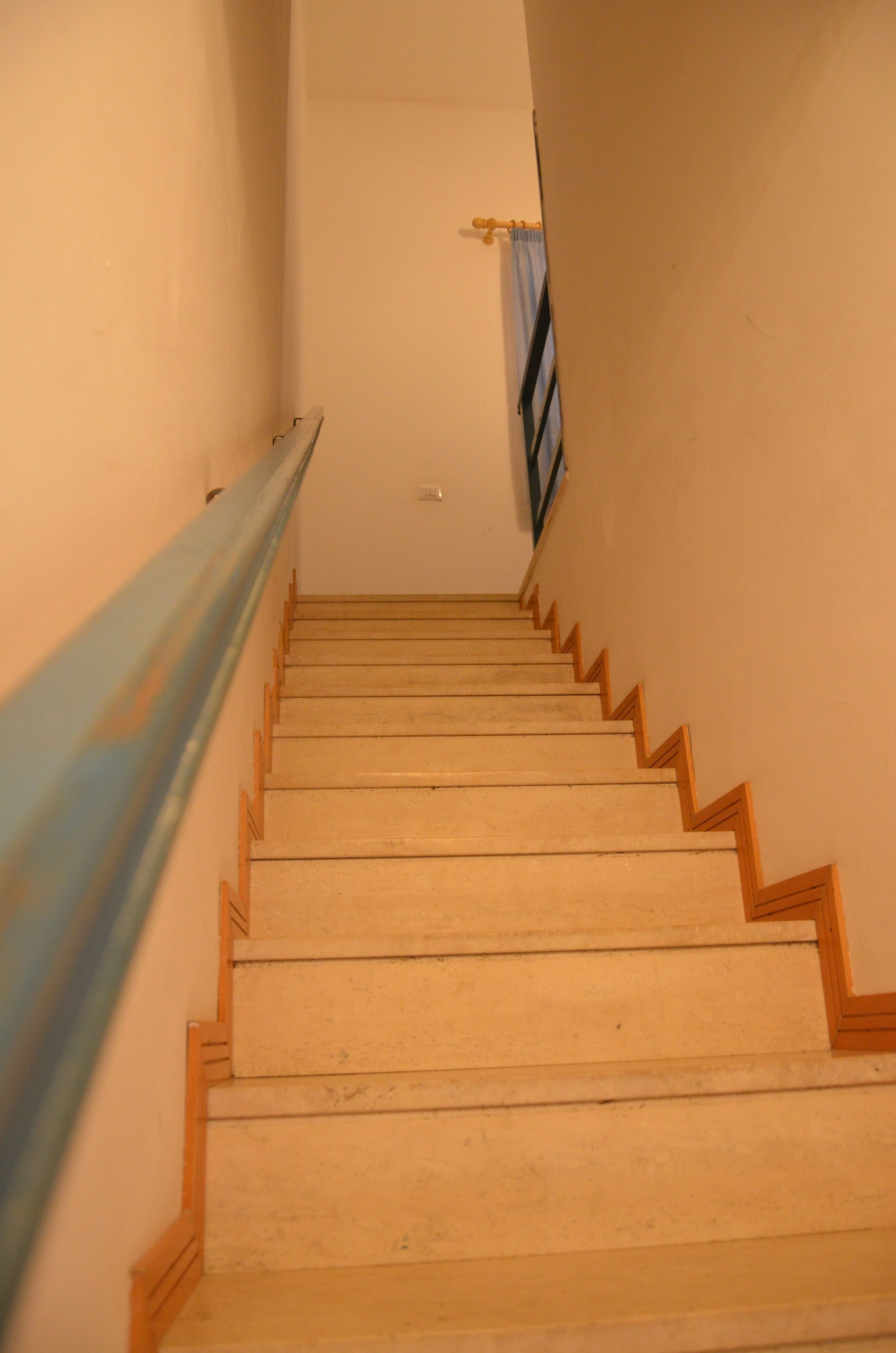 A wooden staircase with a handrail on the left and a curtain on the right.