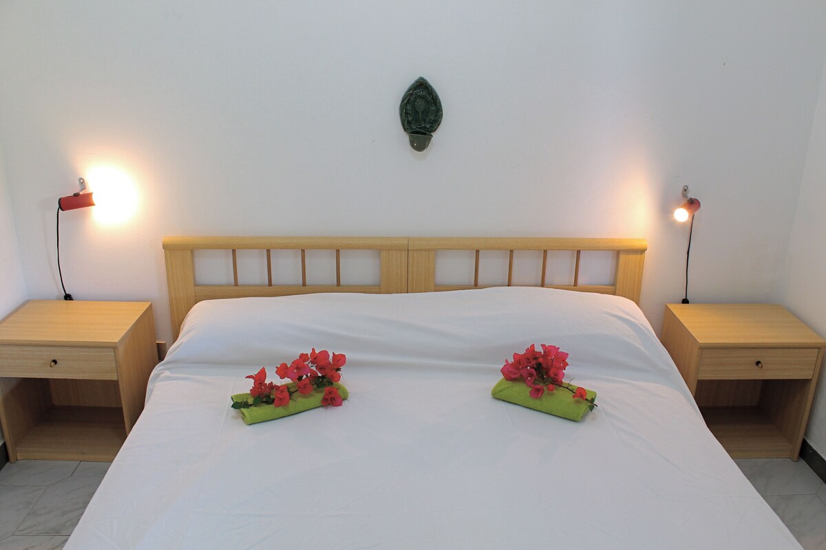 Un lit bien fait, avec des draps blancs, deux tables de chevet avec des lampes et des coussins décoratifs ornés de motifs floraux.
