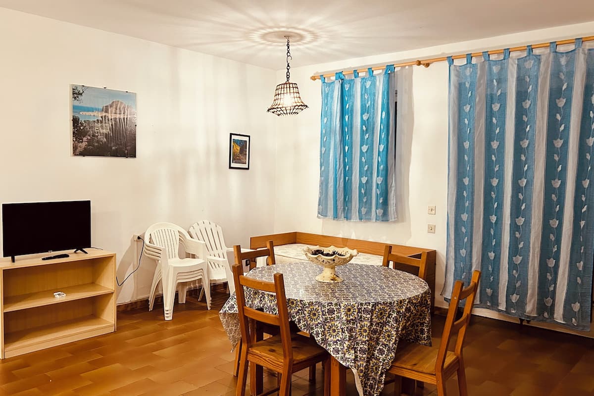 Uma área de refeições com uma mesa redonda, cadeiras, uma televisão e um lustre.