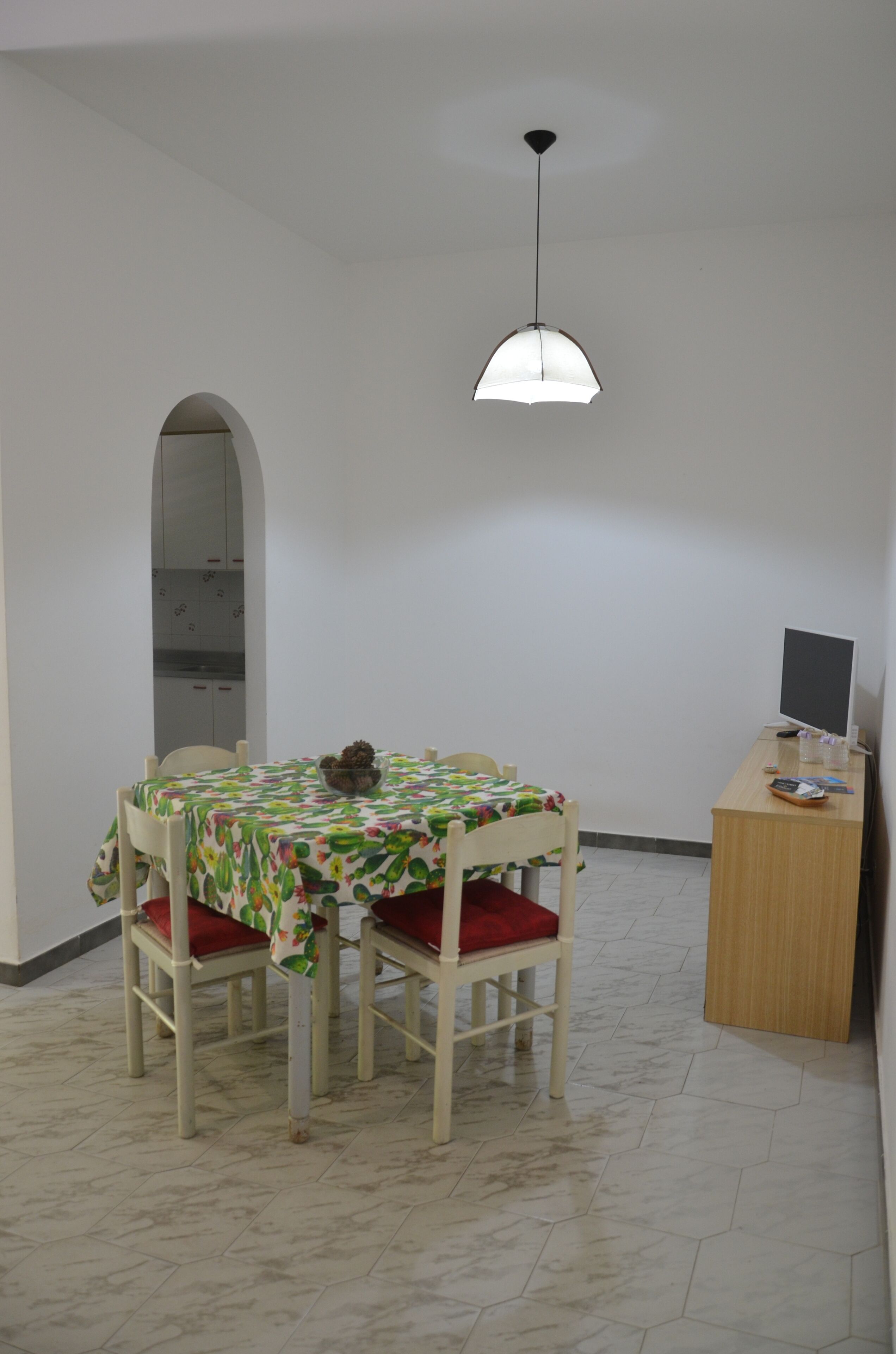 A dining area with a table and chairs, a small plant, and a desk with a computer.