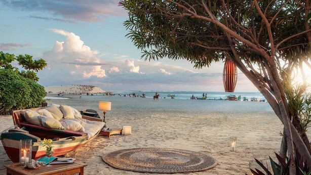 Eine Strandkulisse mit einem Boot, einer Couch und einer Lampe im Sand.