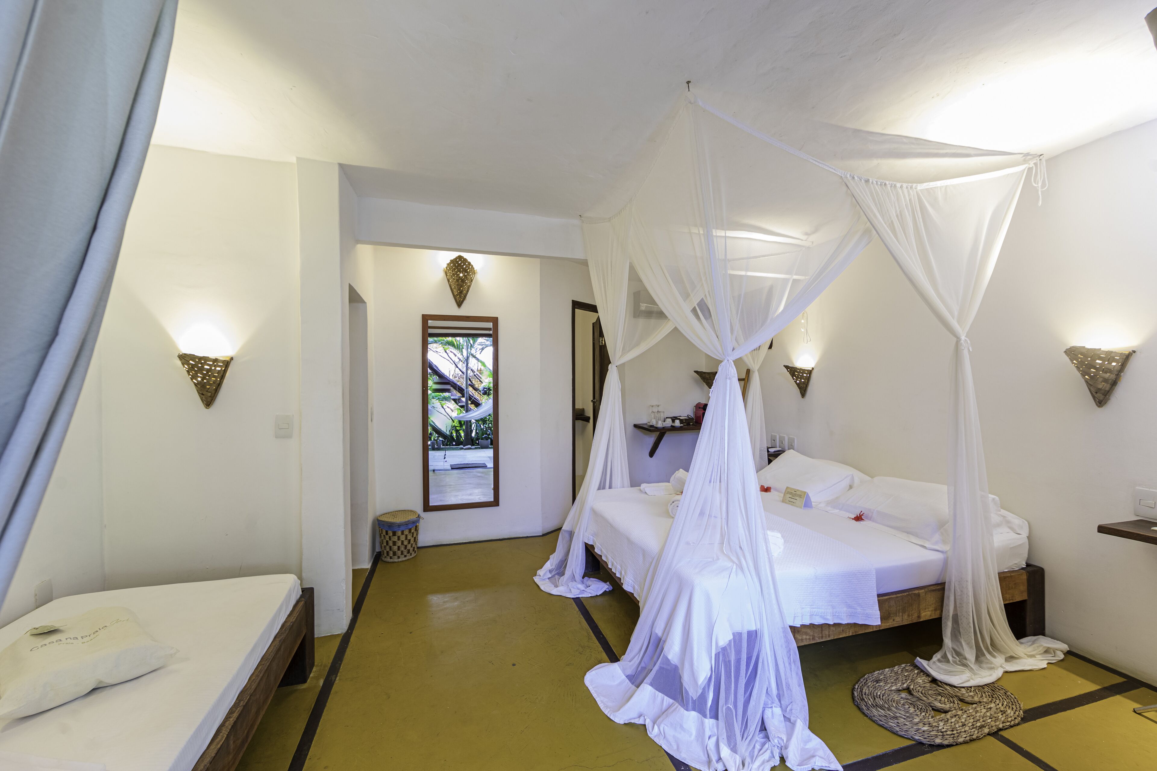 Una habitación con una cama bajo un dosel, una mesita de noche, una lámpara de pared y una puerta que da a otra habitación.