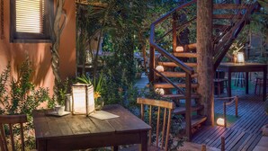 Eine Holzterrasse mit Wendeltreppe, umgeben von üppiger Vegetation und einem rustikalen Gebäude.