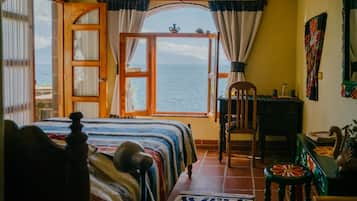 Een kamer met een bed, een houten stoel, een klein tafeltje en uitzicht op zee door een open deur.