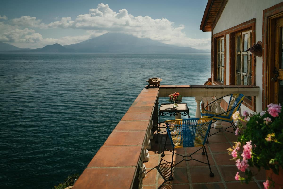 A terrace with a table and chairs overlooking a body of water and distant mountains.