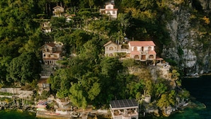 An aerial view of a coastal property with multiple buildings, a dock with boats, and lush greenery. - Hotel y Cafe La Casa del Mundo (Santa Cruz La Laguna)
