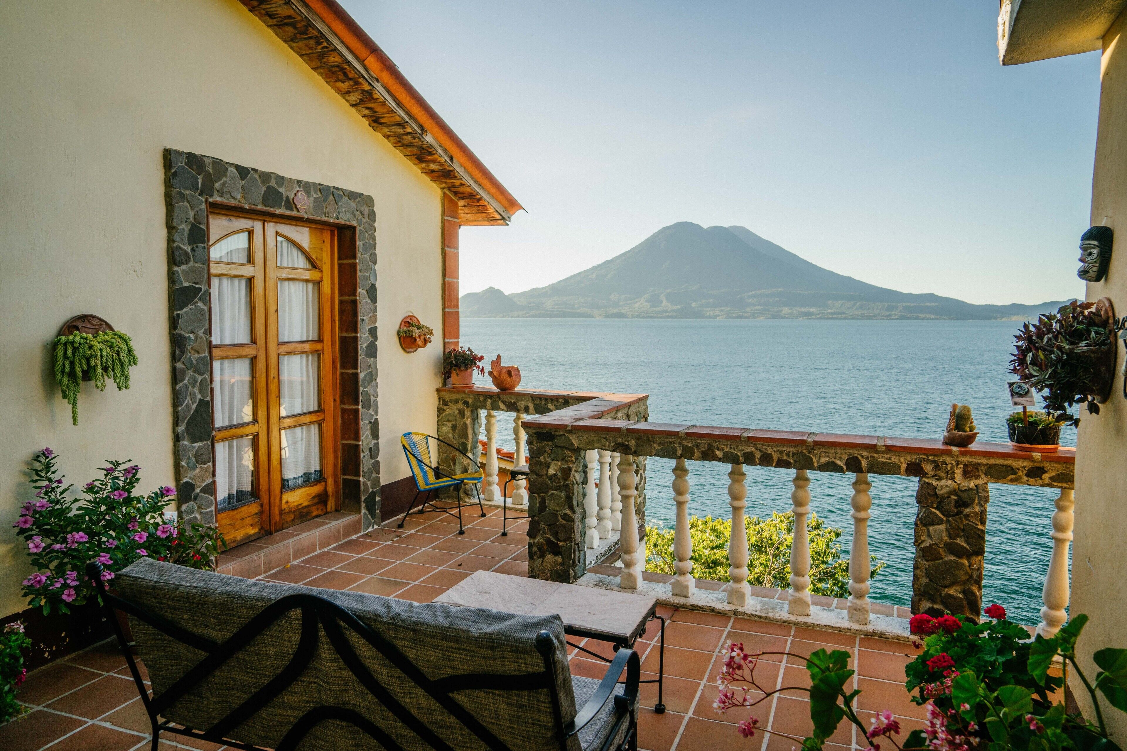 A balcony with a stone wall, a wooden door, and a view of a mountain and water.