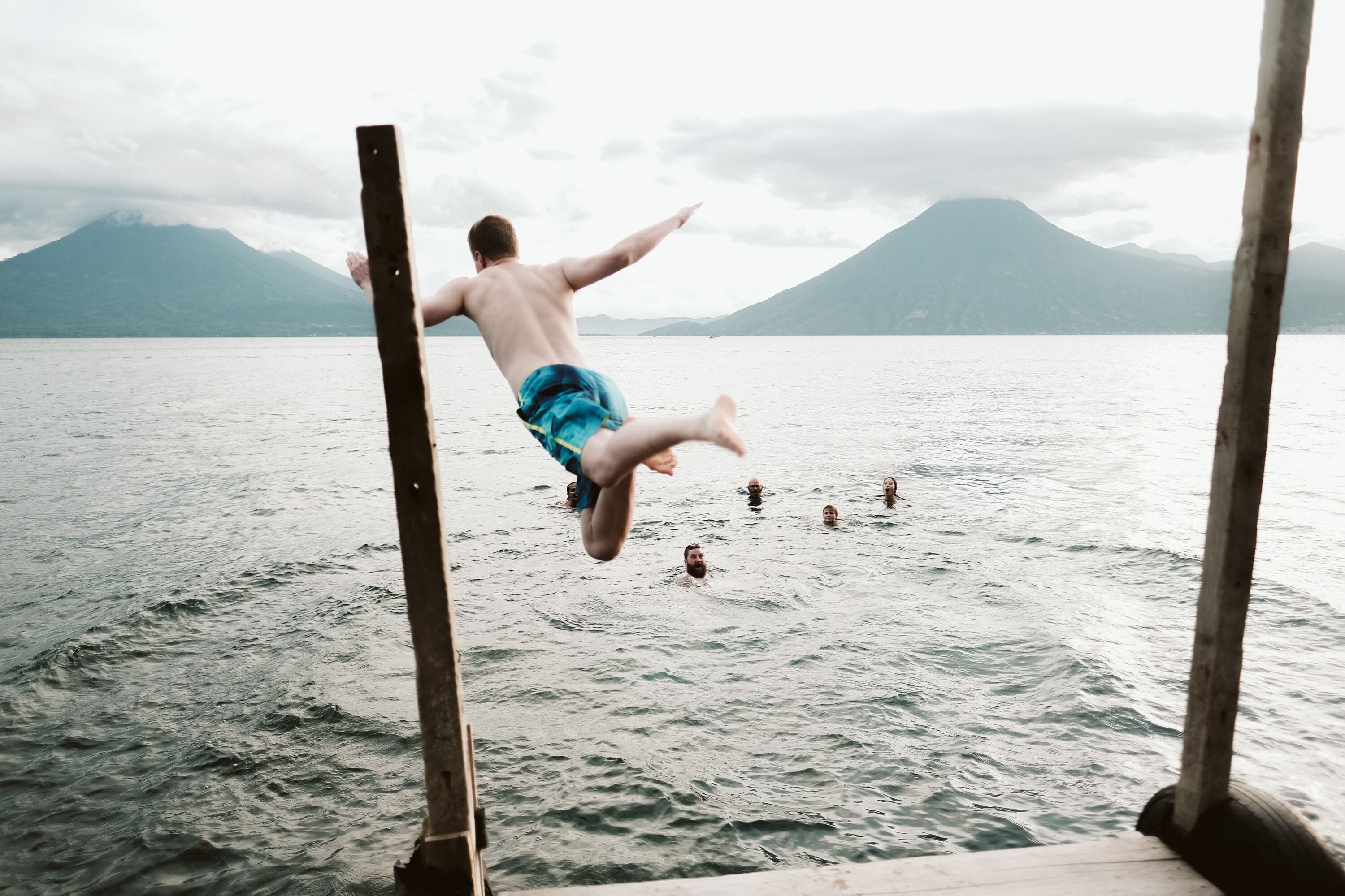 A person jumping off a dock into a lake with mountains in the background.