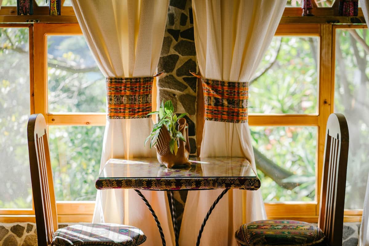 A room with a table, chairs, a potted plant, and a window with curtains.