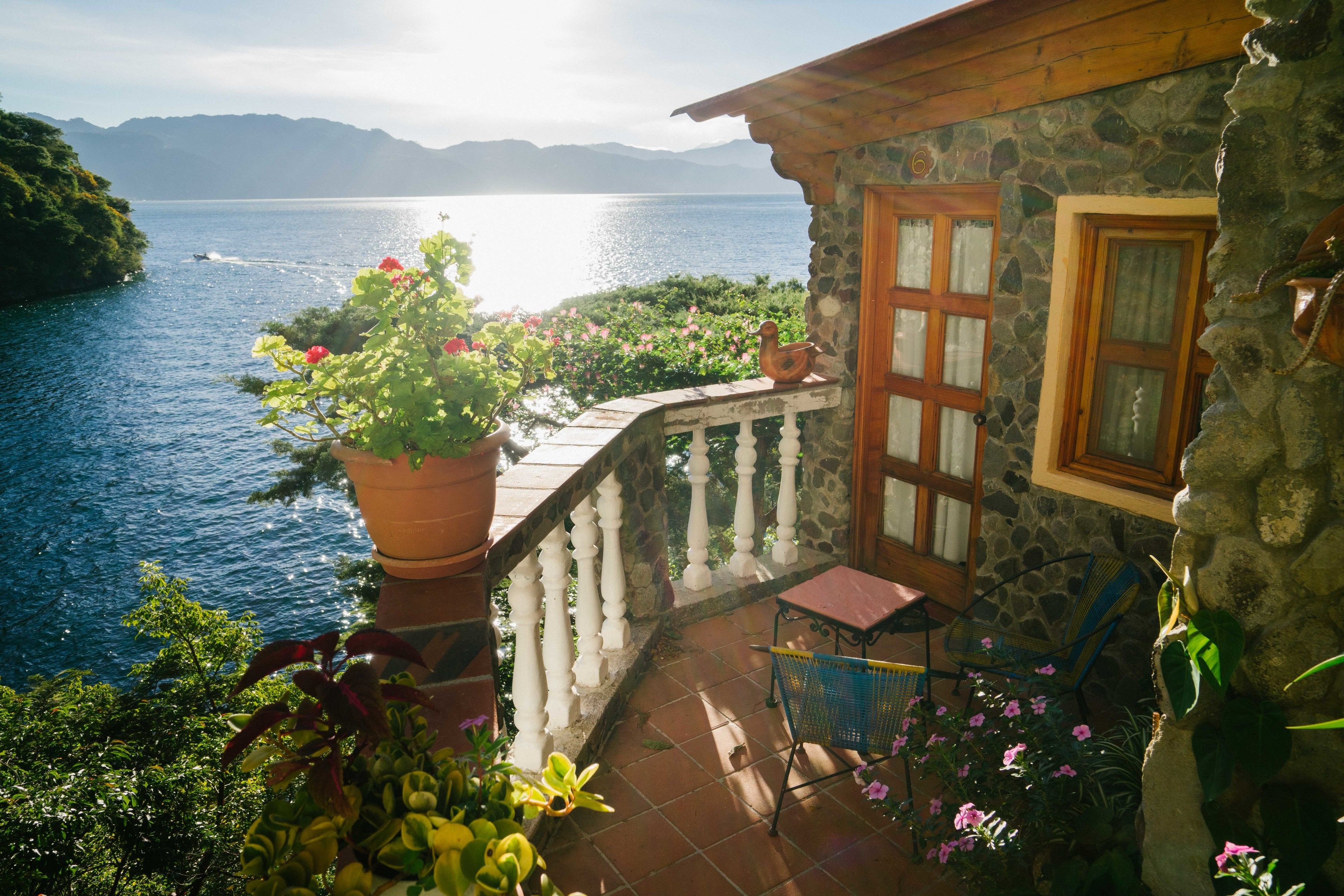 A stone building with a balcony overlooking a lake, a chair, and potted plants.