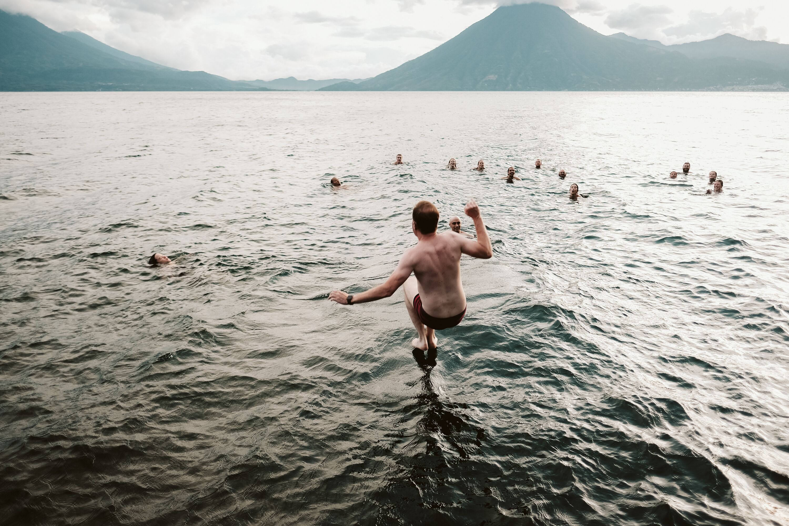 A man jumping into a lake surrounded by mountains.