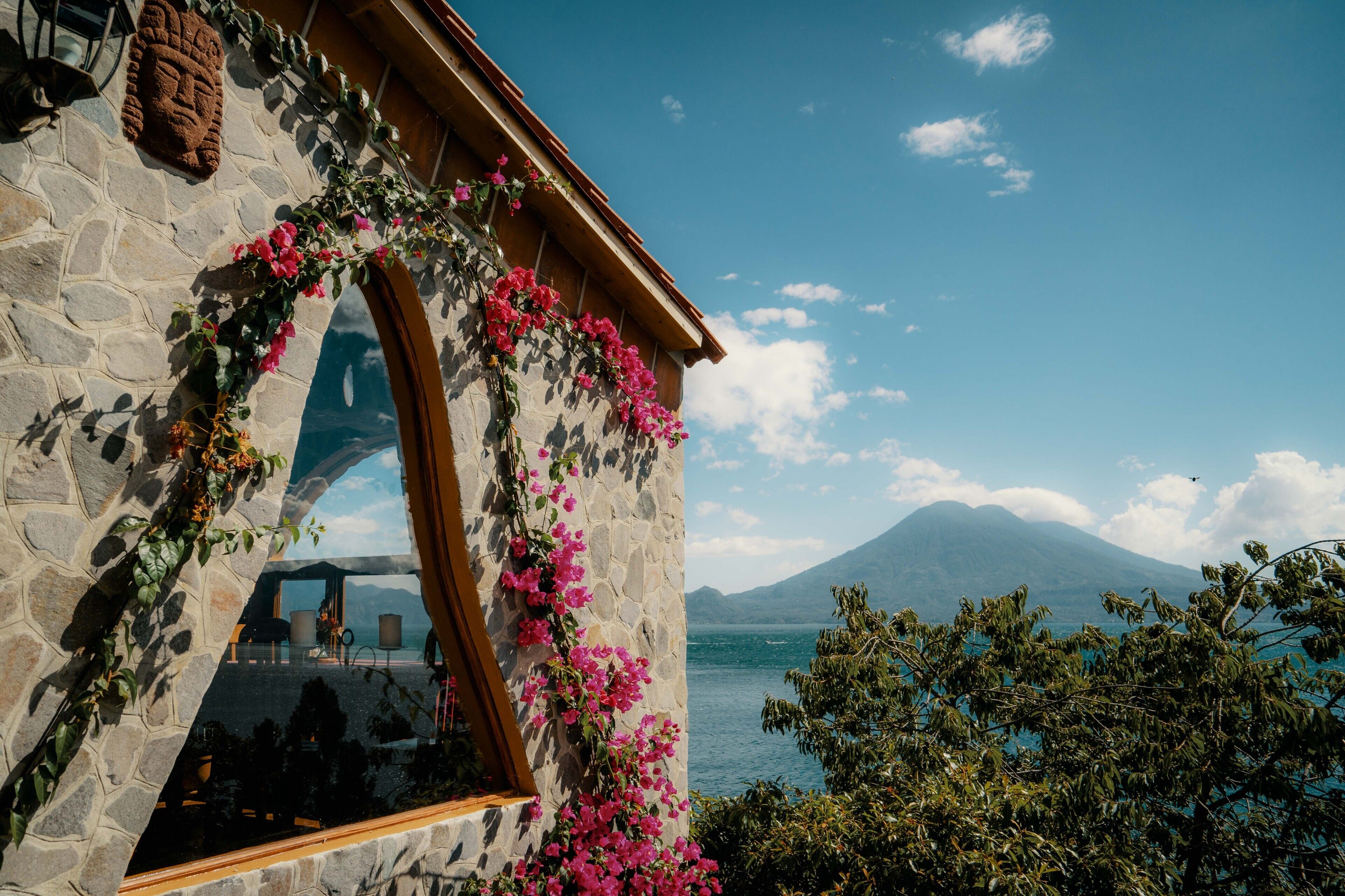 Un edificio de piedra con un arco de madera y flores rosadas.