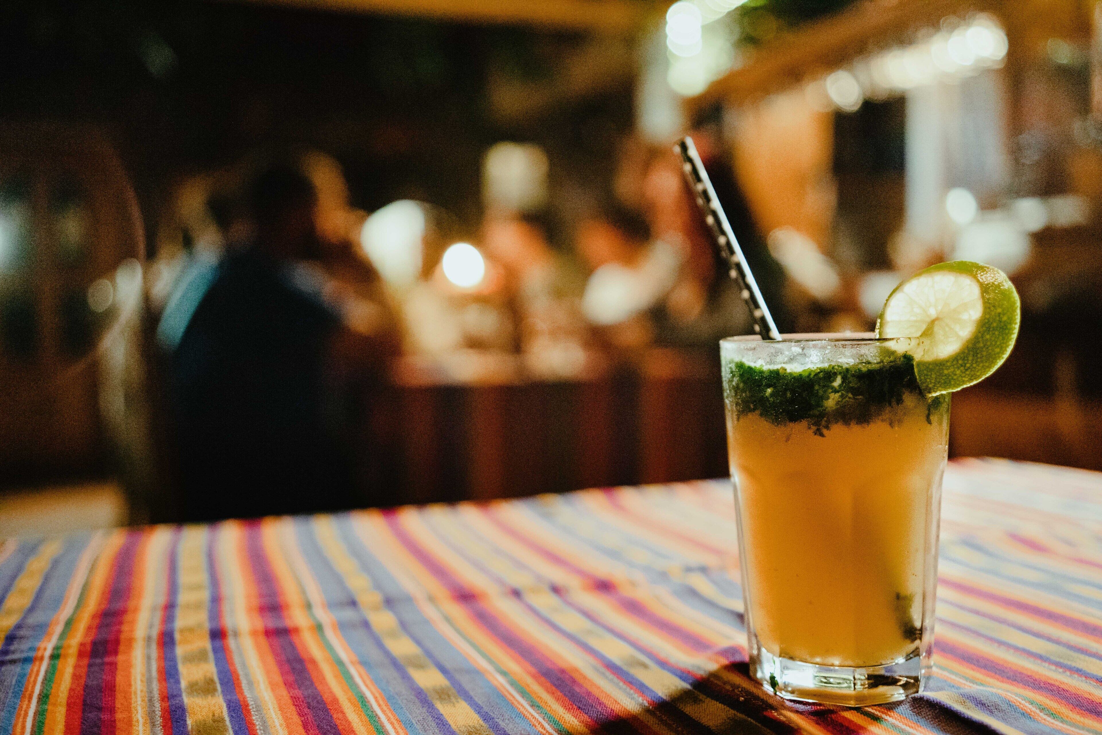 A glass of drink with a lime slice on a striped tablecloth.