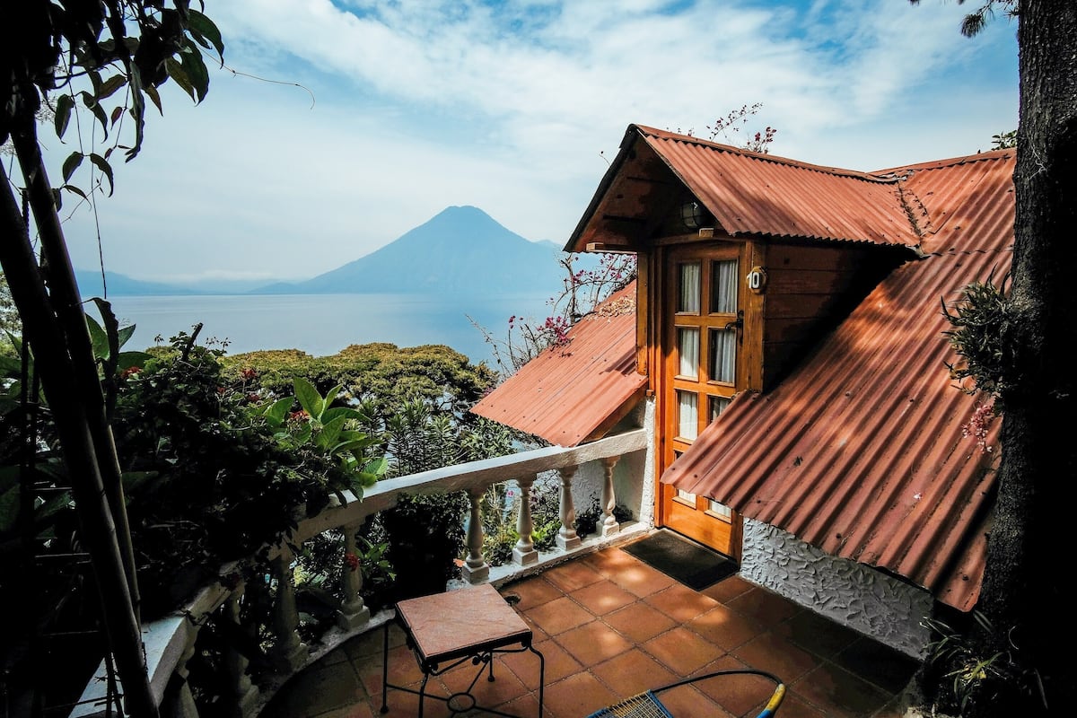 A wooden house with a red roof, a balcony, and a view of a mountain and lake.