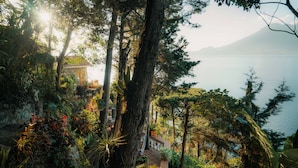 A lush garden with a stone house and a view of the sea. - Hotel y Cafe La Casa del Mundo (Santa Cruz La Laguna)