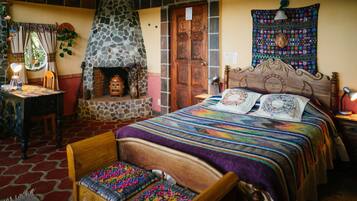 A cozy room with a stone fireplace, a bed with a colorful quilt, a wooden headboard, and a small table with a lamp.