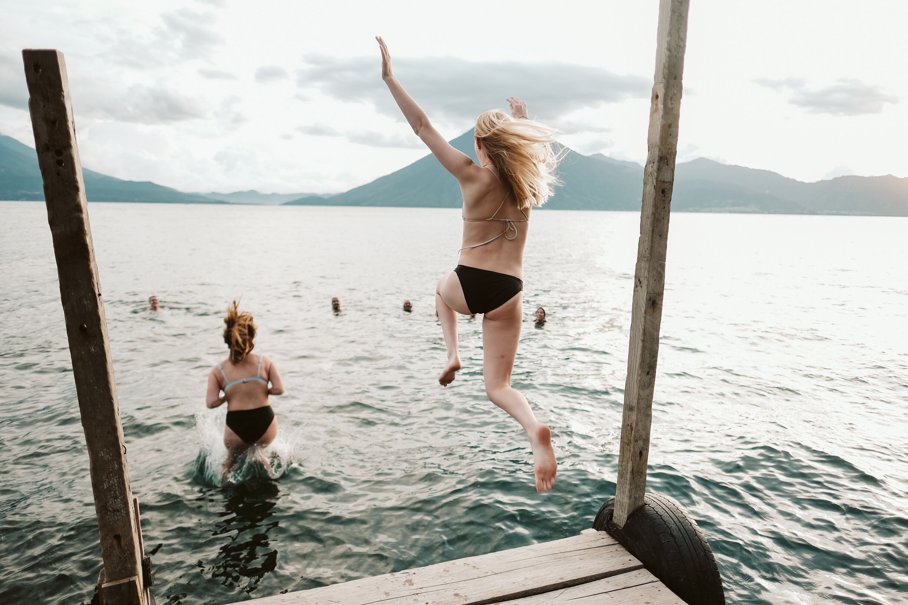 A wooden dock extending into a lake with people swimming and jumping into the water.