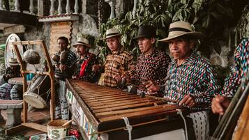 A group of people playing marimbas outdoors, with a stone balustrade and lush greenery in the background.