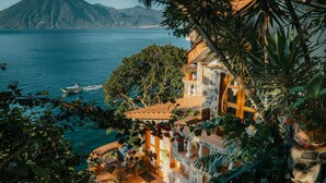 A coastal property with a stone terrace, potted plants, and a view of the sea and mountains. - Hotel y Cafe La Casa del Mundo (Santa Cruz La Laguna)