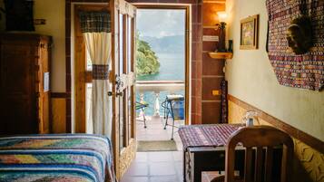 Una habitación con cama, una mesa y vistas a un lago y montañas a través de una puerta abierta.