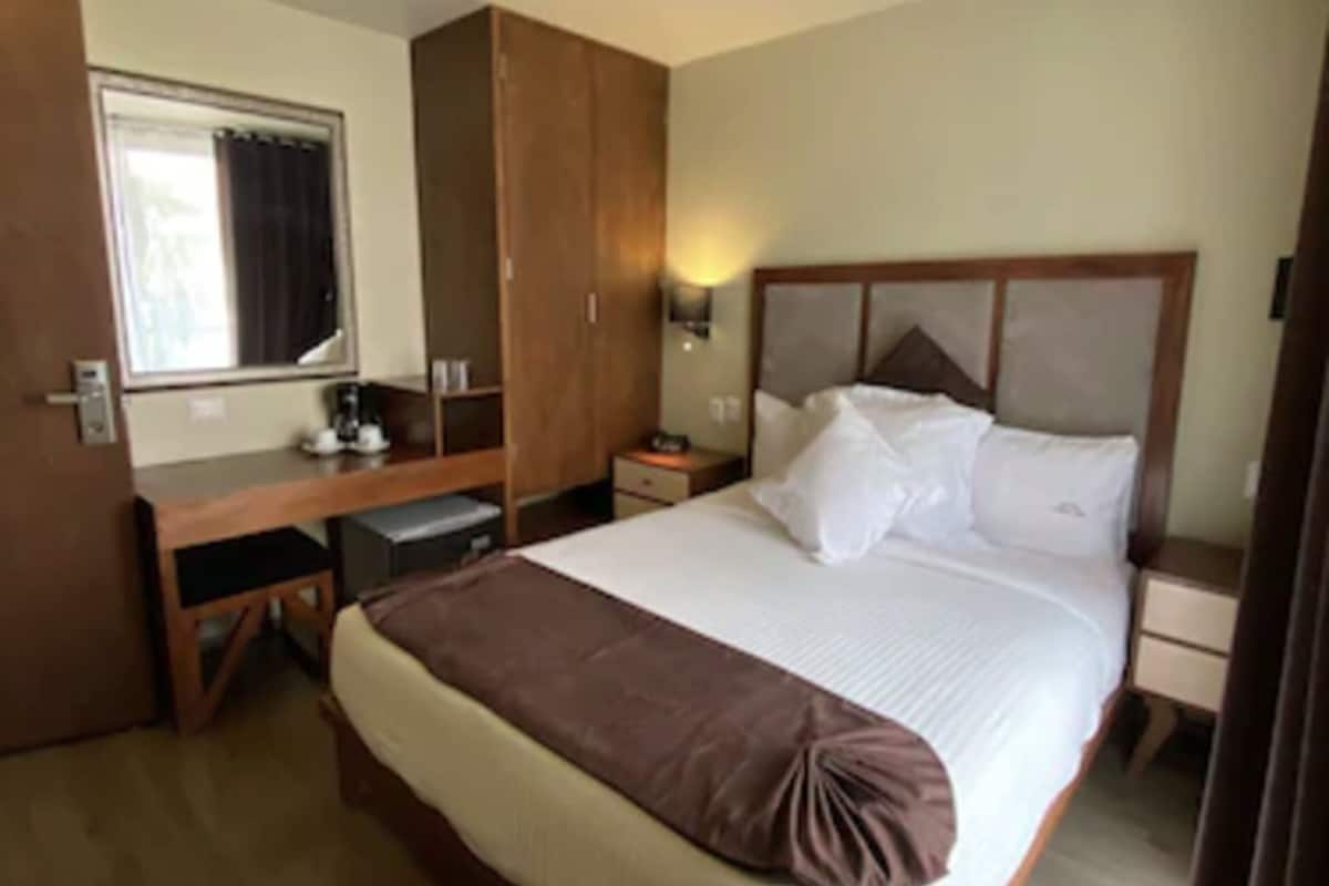 A hotel room with a bed, a desk, a wardrobe, and a nightstand.