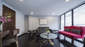 A modern living room with a dark tiled floor, a round glass coffee table, a red sofa, a grey sofa, and a wooden side table with a vase of flowers. - Suites Lerma (Mexico City)