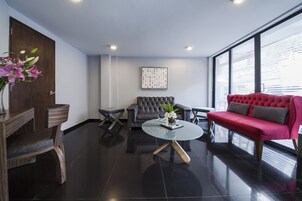 A modern living room with a dark tiled floor, a round glass coffee table, a red sofa, a grey sofa, and a wooden side table with a vase of flowers.