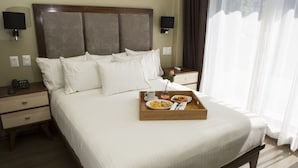 A neatly made bed with white linens, a wooden bedside table with a phone and a lamp, and a tray with breakfast items on the bed. - Suites Lerma (Mexico City)