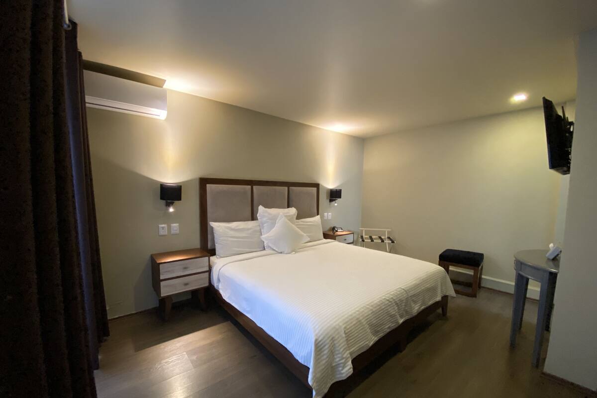 Une chambre à coucher avec un grand lit, des tables de chevet, une commode, un bureau et un téléviseur fixé au mur.