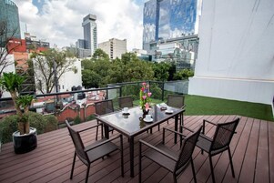 A rooftop terrace with a glass balustrade, a table with chairs, and a potted plant.