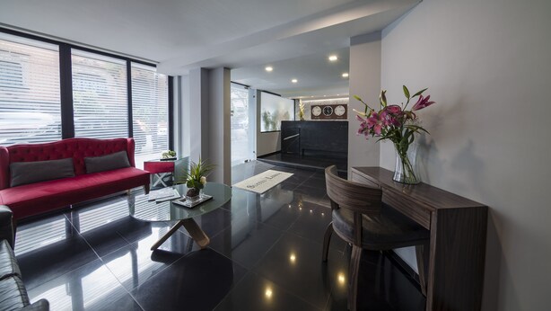A modern living room with a red sofa, a coffee table, and a wooden side table with a vase of flowers. - Suites Lerma (Mexico City)