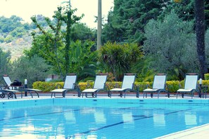 A swimming pool with lounge chairs and a variety of greenery in the background. - Relais il Castello (Monte Castello di Vibio)