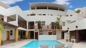 A multi-story building with a pool, outdoor seating, and potted plants. - Hotel Plaza Tangolunda (Santa María Huatulco)