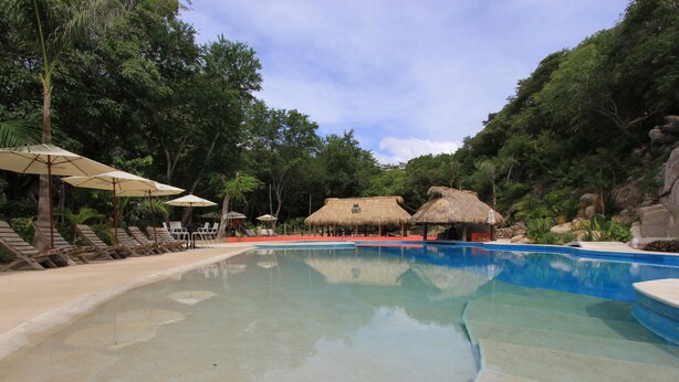 A swimming pool with lounge chairs and thatched-roof structures. - Hotel Plaza Tangolunda (Santa María Huatulco)