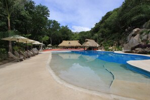 Uma piscina com espreguiçadeiras e estruturas com telhado de palha.
