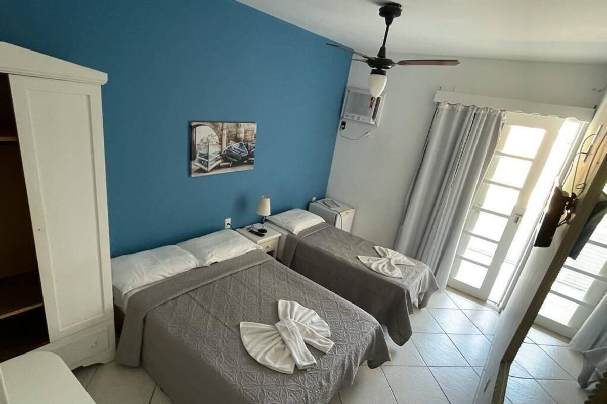 A hotel room with two beds, a ceiling fan, a painting on the wall, and a window with curtains.