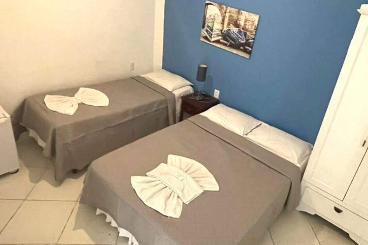 A room with two beds, each with a white bow on the bedspread, a nightstand with a lamp, and a picture on the wall.